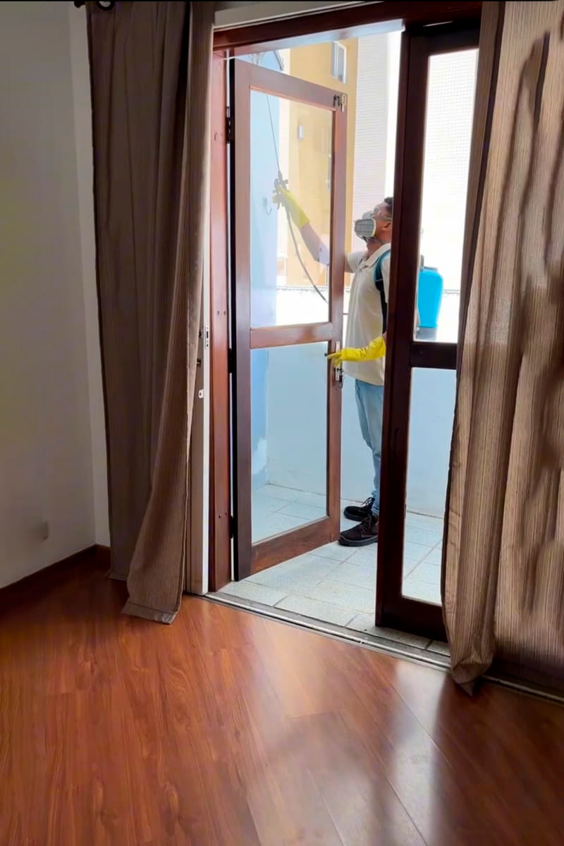 Técnico especializado dedetizando sacada de apartamento em Curitba com pulverizador e EPIs. Serviços profissionais de controle de pragas.